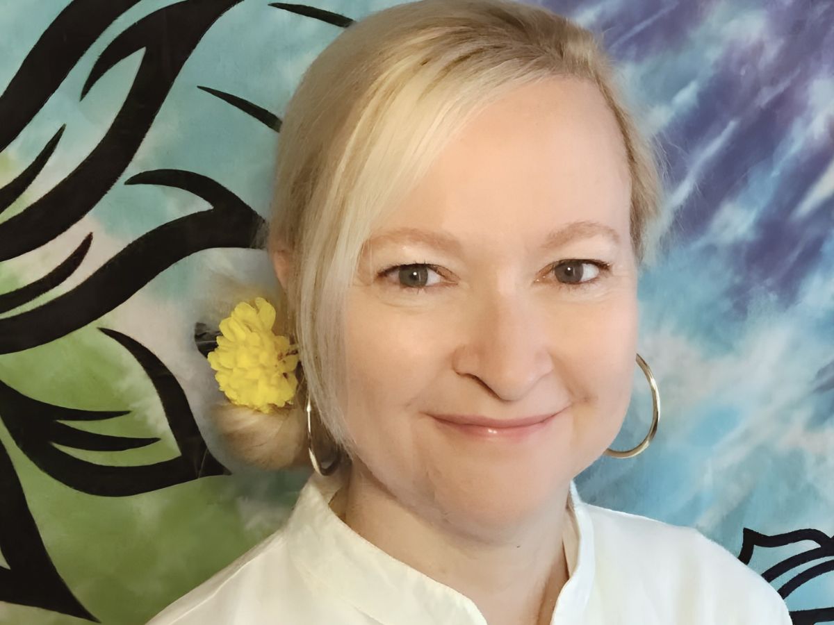 Dorian Lynn, RN, Reiki Master, and Intuitive Mystic Healer, smiling with yellow flower in hair against colorful tapestry