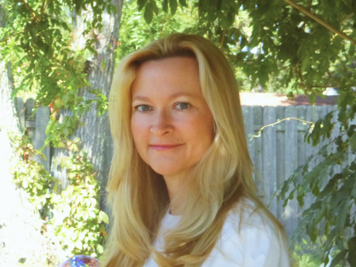 Dorian Lynn, RN and Reiki Master, smiling outdoors in a sunlit garden holding a crystal ball