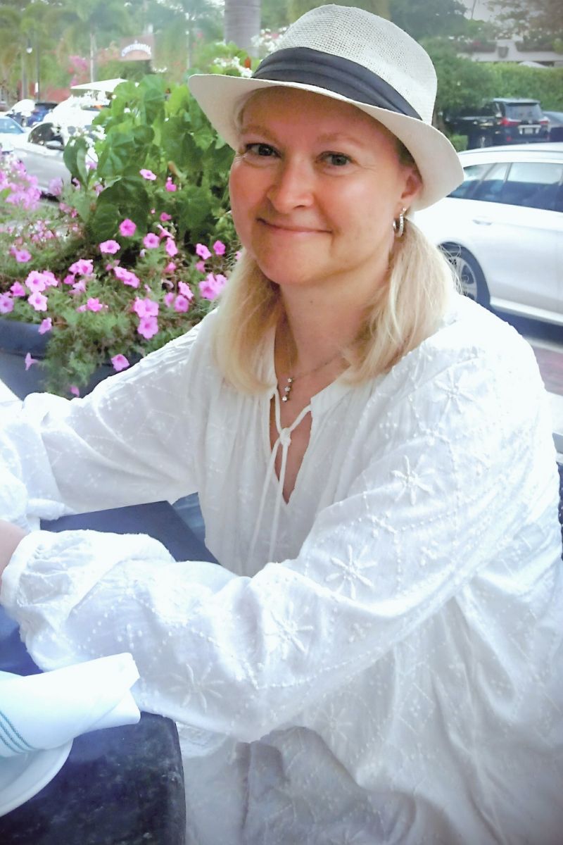 Dorian Lynn, spiritual wellness educator and Registered Nurse, wearing a white hat at an outdoor café